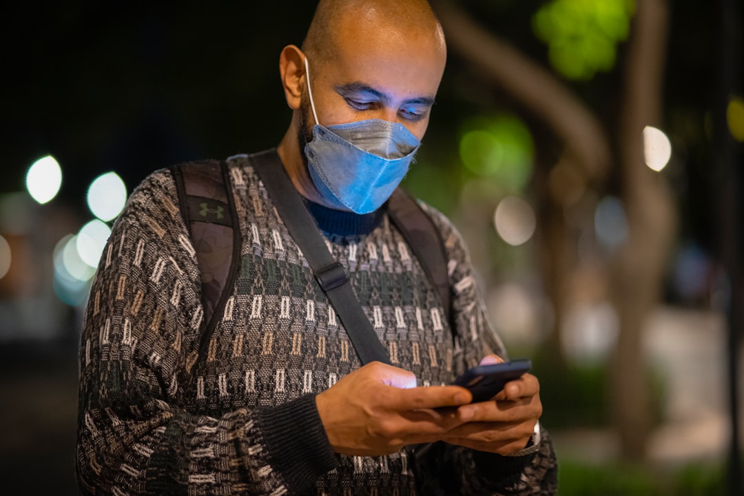 a man wearing a face mask looking at his cell phone